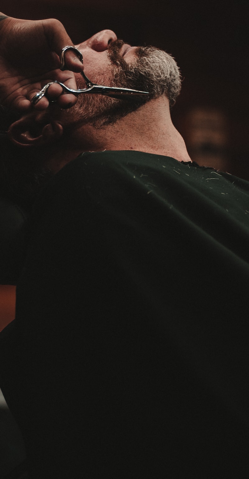 Close on a barber's hands trimming a reclined customer's beard with scissors