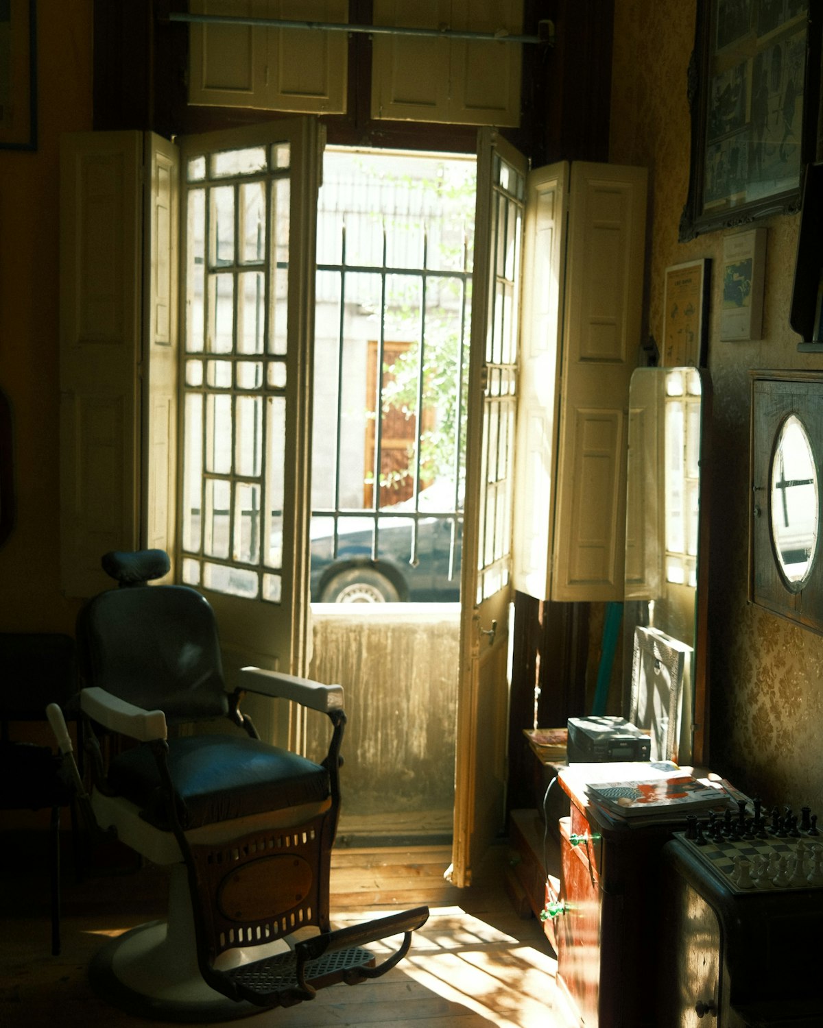 The shop door propped open onto the street, sunlight across the floor and a chair beside it