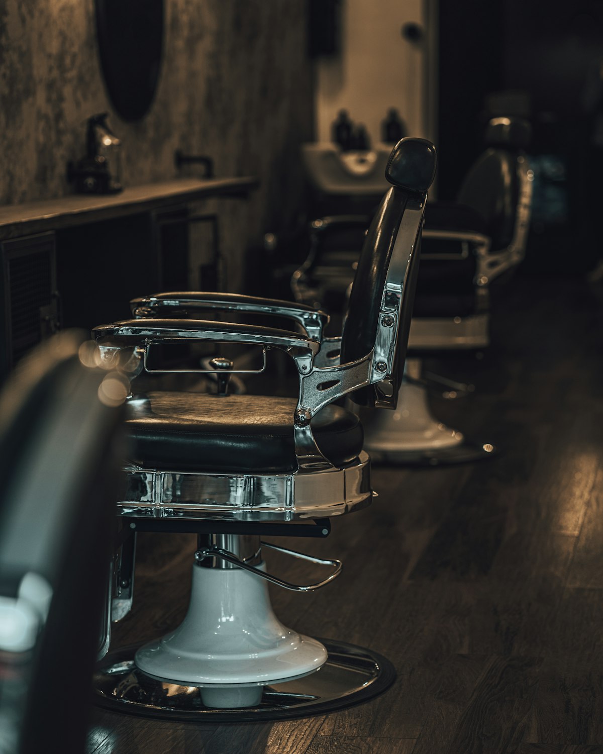 A chrome barber's chair standing alone on the shop floor, the room dark behind it